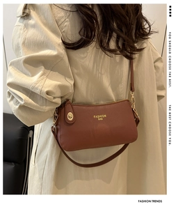Detail of brown litchi pattern shoulder bag with gold hardware on a beige trench coat