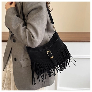 Detail of black suede shoulder bag featuring long fringe tassels and gold buckle accents
