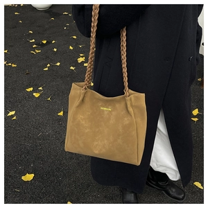 Detail of tan suede tote bag with woven shoulder straps and gold lettering on the body