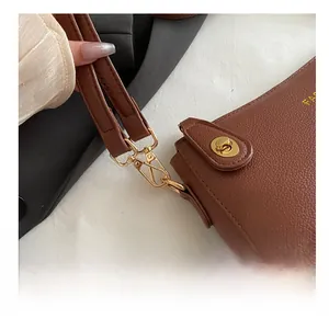 Close-up of golden metal hooks and lychee grain leather on a brown crossbody bag