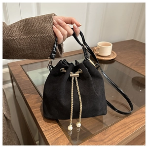 Detail of black suede bucket bag featuring drawstring closure with pearl chain pendant