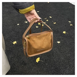 Detail of vintage matte brown suede shoulder bag with gold hardware held outdoors