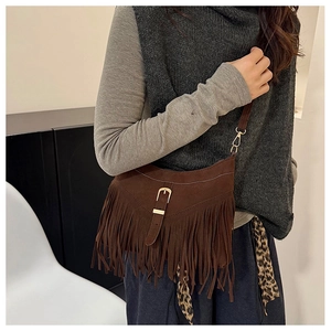 Detail of brown faux suede tassel shoulder bag with retro metal buckle on a female model
