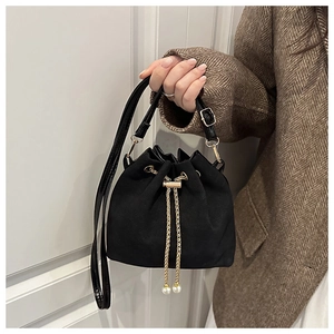 Detail of black drawstring bucket bag with gold chain and pearl accents on tweed coat
