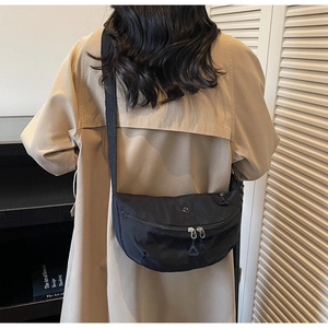 Détail du sac bandoulière en nylon noir porté avec un trench-coat de couleur kaki