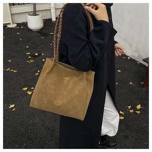 Detail of trendy brown tote bag with woven handles and gold logo against autumn coat