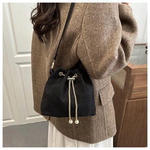 Detailed view of black suede bucket bag with gold chain drawstring and pearl accents