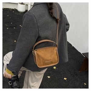 Détail du sac bandoulière en daim marron montrant la poignée et les finitions en métal