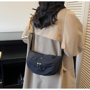 Model wearing a black nylon crescent crossbody bag over a beige trench coat
