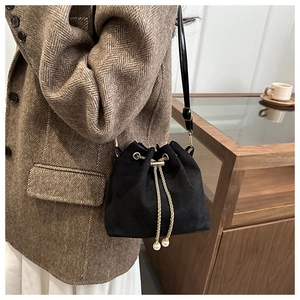 Detail of black suede bucket bag featuring golden chain drawstring and pearl accents
