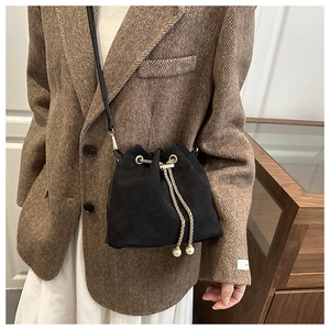 Detail of black suede bucket bag with gold chain, pearl charms and leather strap
