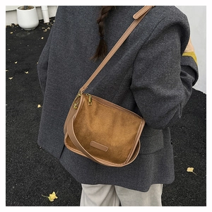 Gros plan d'un sac bandoulière en daim marron porté sur un costume avec feuilles d'automne