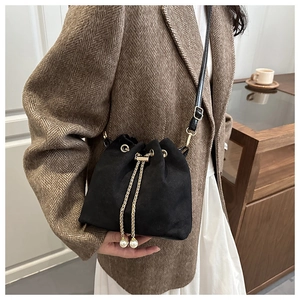 Detail of black drawstring bucket bag with gold chains and pearl charms on a model