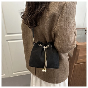 Detail of black suede bucket bag featuring gold chain drawstring and pearl accents