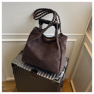 Detail einer dunkelbraunen Wildleder-Tote-Bag mit geflochtenen Griffen auf Koffer