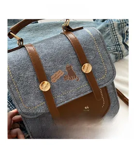 Detail of blue denim and brown leather handbag with a cat print and gold buckle strap
