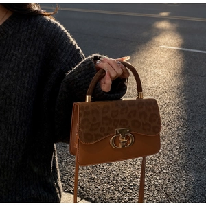 Detailed view of the leopard print flap and golden CD buckle on a brown leather bag