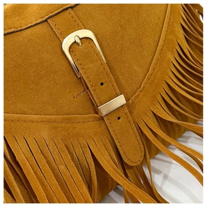 Detail of tan suede tote bag featuring bohemian tassels and polished gold buckle closure