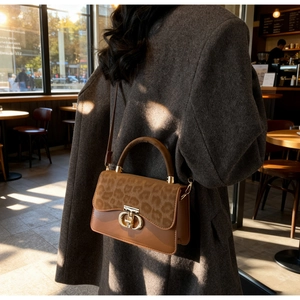 Detail of leopard print leather handbag with gold metal clasp on a brown wool coat