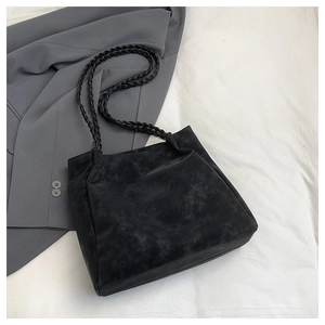 Detailed close-up of a black suede tote bag featuring distinctive woven shoulder straps