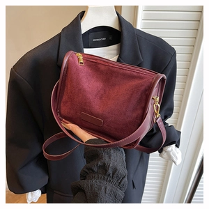 Detail of burgundy frosted suede crossbody bag with gold metal zipper and leather strap