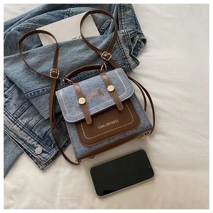 Detail of blue denim backpack with cat illustration and brown leather trim accents