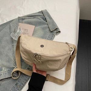 Minimalist beige nylon crossbody bag with adjustable strap shown in a lifestyle setting
