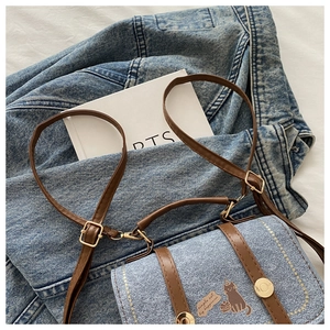 Detail of denim crossbody bag with brown faux leather trim and cartoon cat illustration
