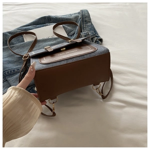 Close-up of retro denim and brown leather crossbody bag with gold metal hardware on bed
