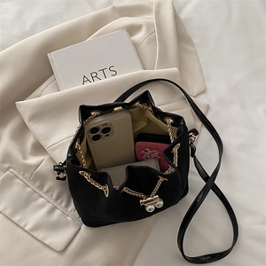Retro black matte bucket bag with gold chain drawstring and pearl accents on beige blazer
