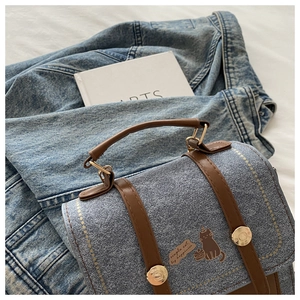 Detail of denim crossbody bag with brown leather trim and cartoon cat illustration
