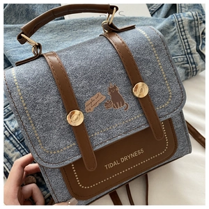 Detail of blue denim and brown leather handbag with cat illustration and metal buckle