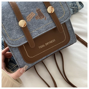 Close-up of blue denim texture and brown leather stitching on a small crossbody bag