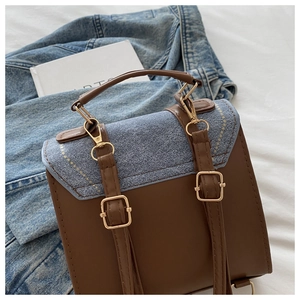 Close-up of retro color-block handbag with blue denim flap and gold metal buckle detail