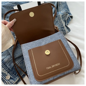 Detail of blue denim and brown leather crossbody bag with white stitching and magnetic flap