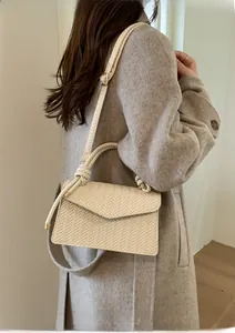 Detail showing woven texture on a cream handbag with a knotted top handle and gold hardware