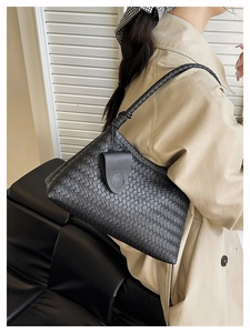 Detail of black woven leather texture on a shoulder bag worn with a beige trench coat