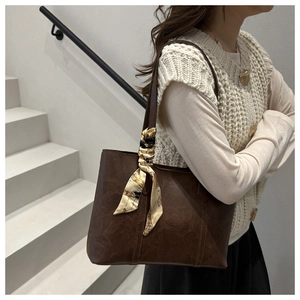 Detail view of a vintage brown tote bag with printed silk scarf on a model shoulder