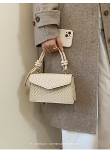 Close-up of cream woven texture handbag with V-shaped patterns and minimalist knot handle