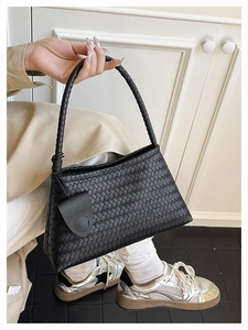 Close-up of black woven leather shoulder bag with round handle and side leather button