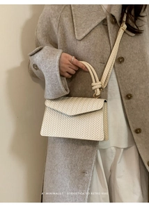 Detail of cream woven shoulder bag featuring a knotted handle and textured flap closure