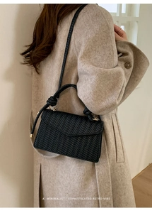Close-up of black woven crossbody bag with wheat pattern texture and knotted handle