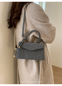 Model wearing a grey leopard print suede handbag with gold accents and shoulder strap