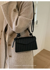 Close-up of black woven texture handbag featuring a unique knotted handle and gold metal hardware