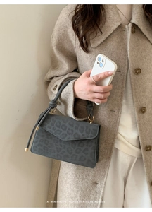 Detail of grey leopard print bag with suede texture and gold hardware on beige coat