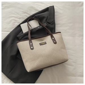 Detail of canvas tote bag with brown leather handles and brand logo patch for office work