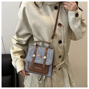 Detailed view of vintage blue denim and brown leather crossbody bag on beige coat