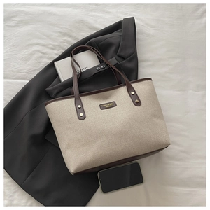 Detail of canvas tote bag with brown leather trim and metal logo on a grey blazer