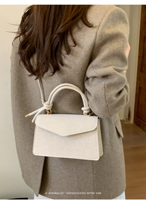 Minimalist beige crossbody bag with knot ring handle shown on a model in wool coat