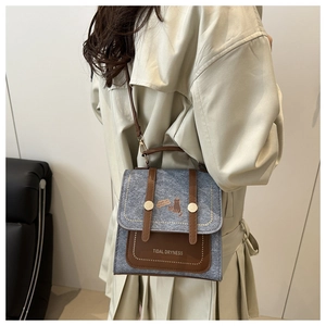 Detail of grey felt and brown leather crossbody bag with cat motif on a beige trench coat
